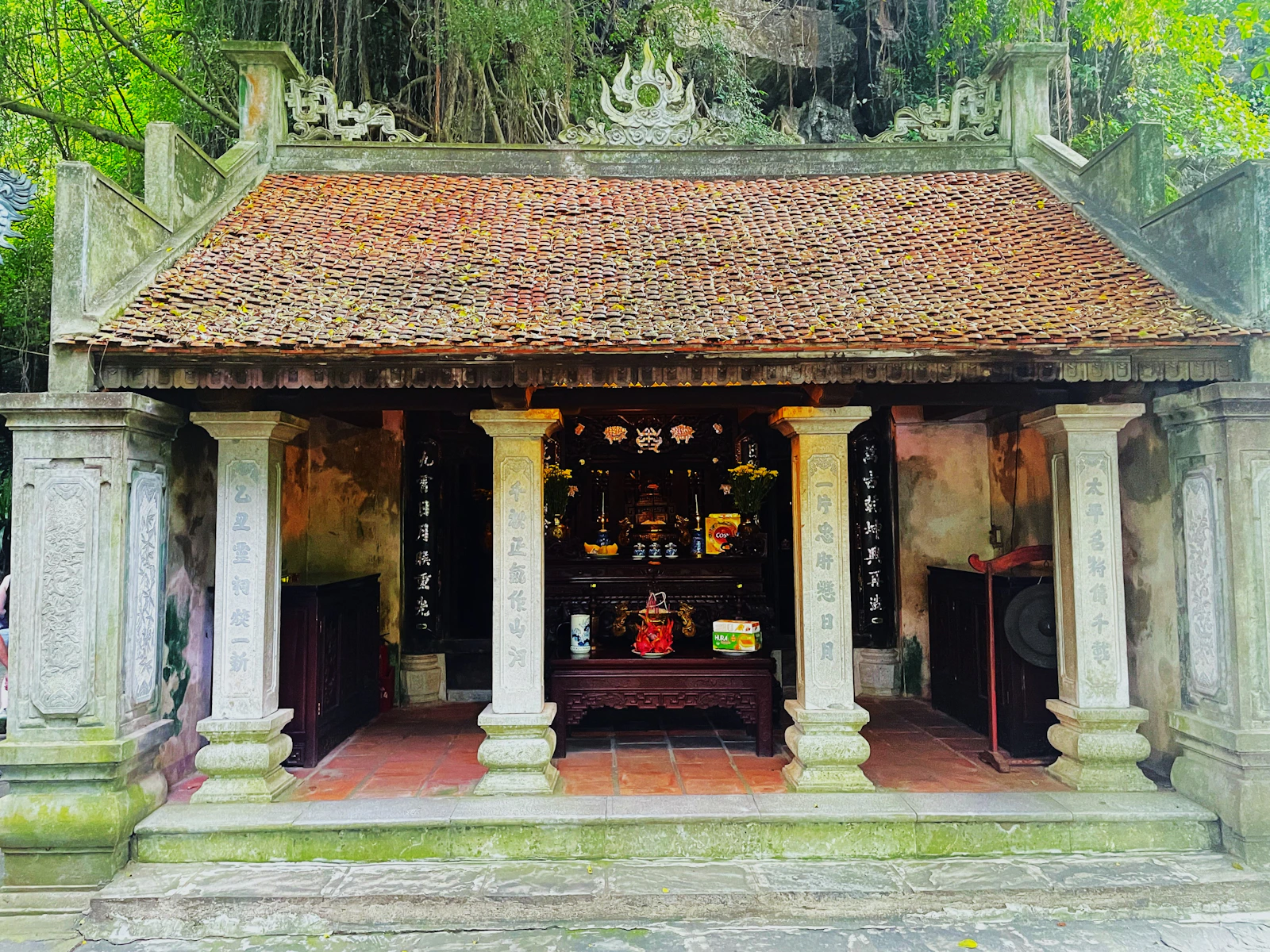 Tempelbau der Bich-Dong-Pagode mit Steinsäulen, Ziegeldach und bewachsenem Fels im Hintergrund