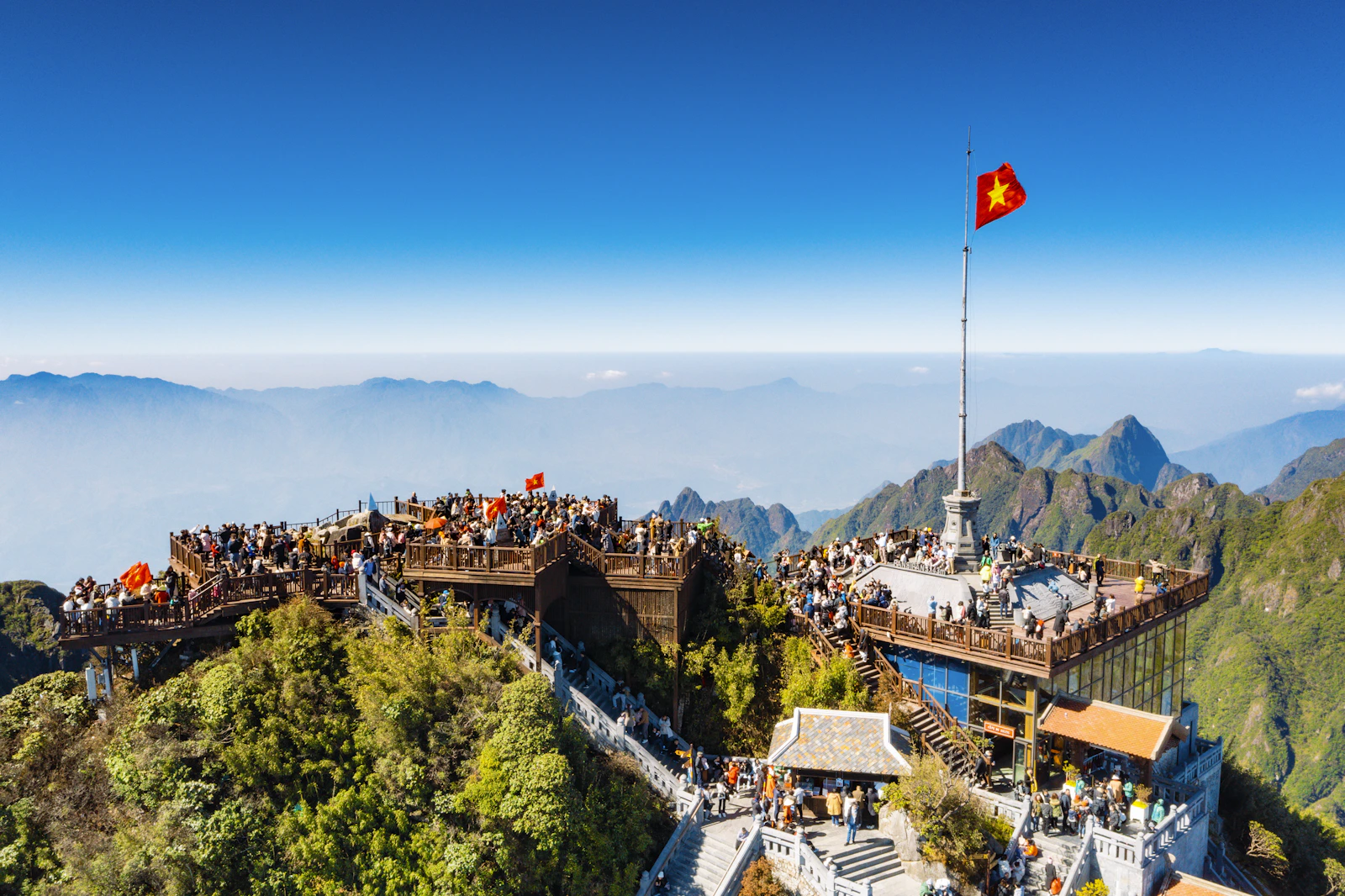 Sonnige Gipfelterrassen des Fansipan mit vietnamesischer Flagge und umliegenden Bergkämmen